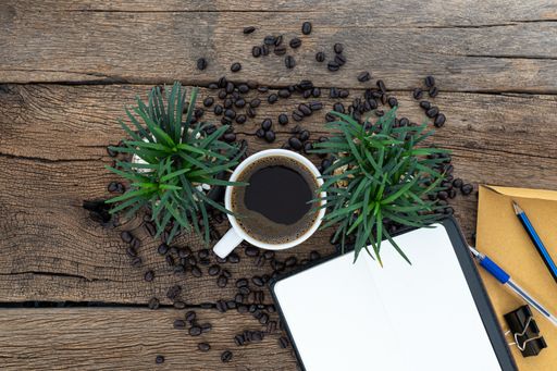 A top view of a cup of coffee with coffee beans and plants on a wooden table