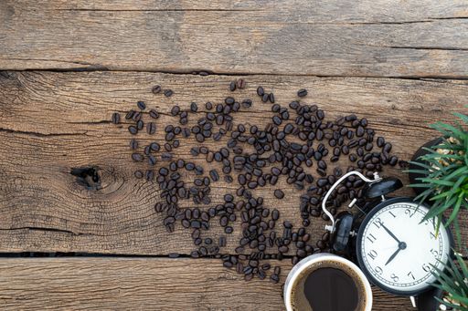A top view of a cup of coffee and coffee beans with a watch on a wooden table