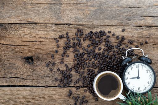 A top view of a cup of coffee and coffee beans with a watch on a wooden table