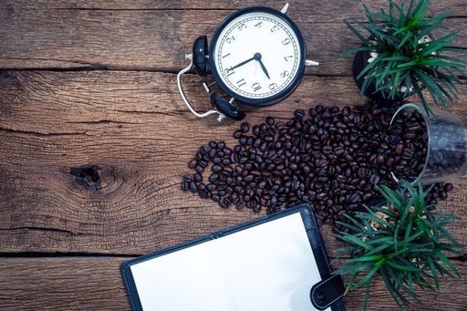A top view of a cup of coffee and coffee beans with a watch on a wooden table