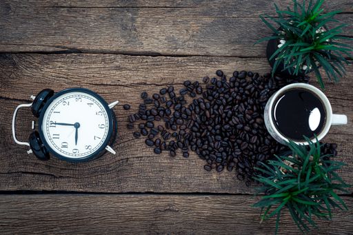 A flat lay shot of an alarm clock, a mug of coffee and coffee beans on a wooden desk