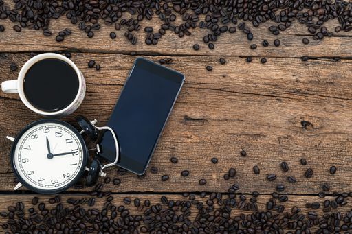 A top view of a cup of coffee with a watch and a smartphone surrounded by coffee beans