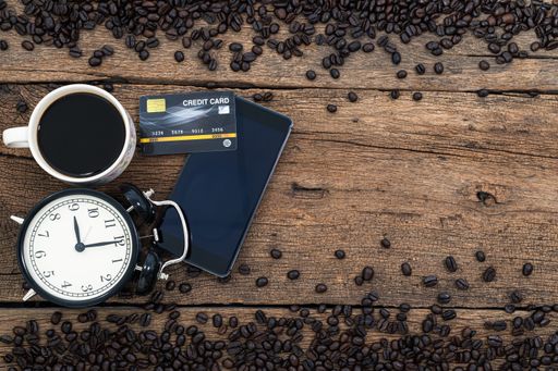 A top view of a smartphone, a credit card and coffee on a wooden desk