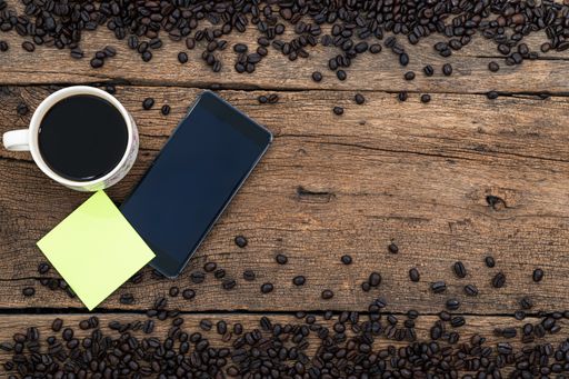 A mobile phone, sticky notes, a cup of coffee and roasted beans on a wooden surface
