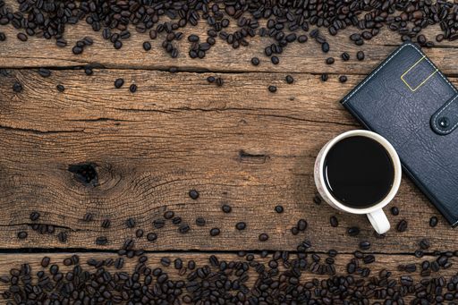 A top view of a cup of coffee, a notebook and roasted beans on a wooden surface