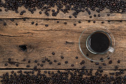 A top view of a cup of coffee and roasted beans on a wooden surface