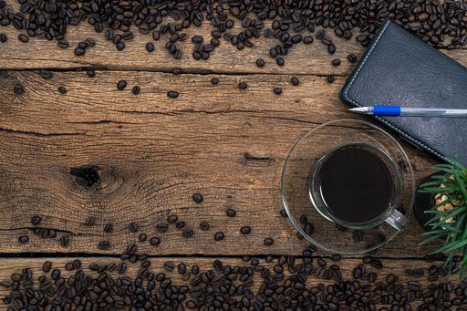 A top view of a cup of coffee with a notebook on a wooden table with roasted coffee beans