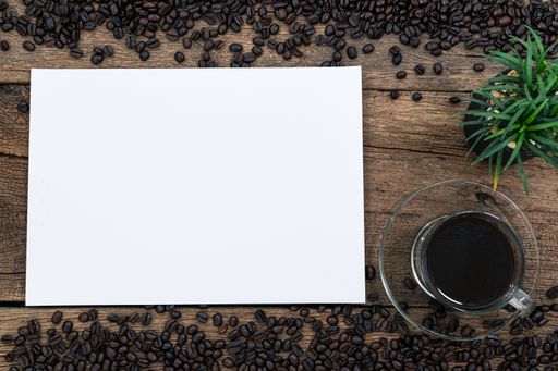 A top view of a blank paper, a cup of coffee and coffee beans on a wooden desk