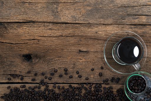 A top view of a cup of coffee and roasted beans on a wooden surface