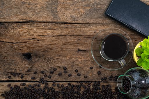 A top view of a cup of coffee on a wooden table surrounded by coffee beans