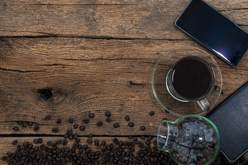 A top view of a smartphone and coffee on a wooden desk