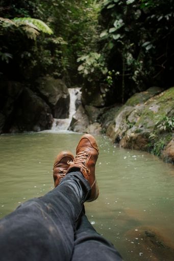 A vertical shot of male feet on the background of a beautiful waterfall in a forest