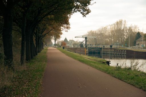 A scenic view of a bike lane next to green trees and a river in Helmond, Netherlands