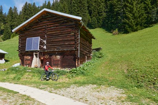 A cyclist passing beside an old wooden cabin decorated with deer skulls on a sunny day in the countryside