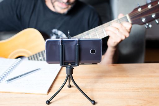 A man having a remote online guitar lesson via a video conference using a smartphone on a phone mount