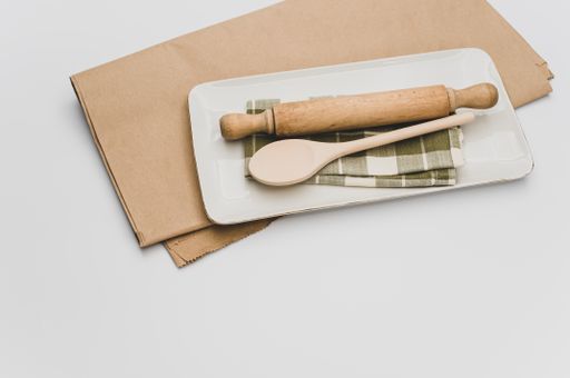 finely decorated stoneware dish and wooden kitchen tools on a brown paper and white background