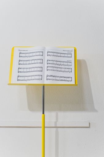 yellow music stand with music paper sheets in front of white wall