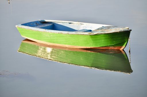 An amazing shot of a green fishing boat on a calm reflective lake background