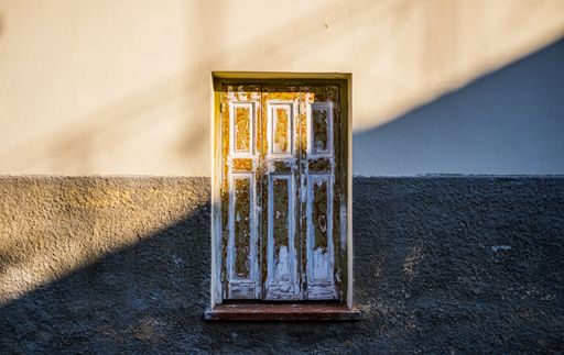 An old weathered grungy wooden window of a concrete house during the sunrise