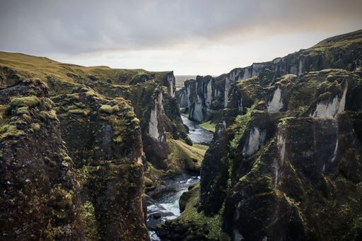 Aerial view of Fjadrargljufur  canyon in Iceland with lush green cliffs and a winding river under a cloudy sky.
