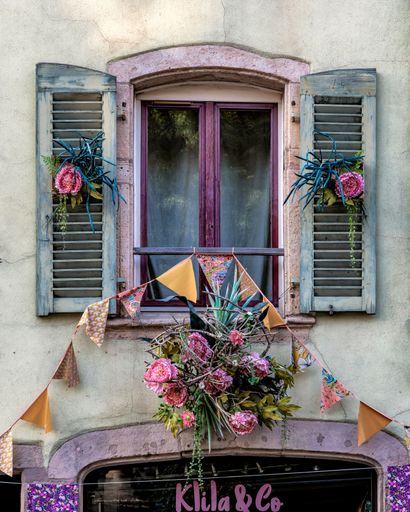 Charming window with blue shutters, floral decorations, and colorful bunting in a quaint European setting.