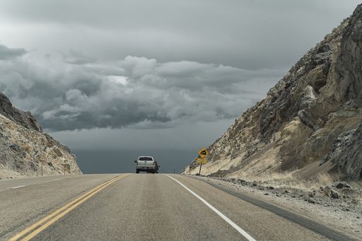 A car on the U.S. 95 asphalt highway in Southern Idaho under a gray sky with large massive clouds