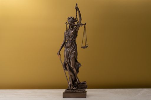 A bronze statue of a woman with scales as the symbol of law and justice on a golden background