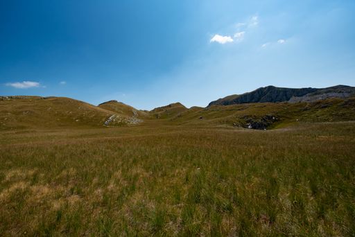 A beautiful shot of a field and mountains under a blue cloudy sky on a sunny day