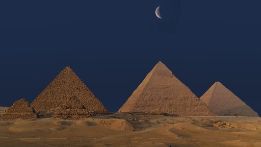 The Pyramids of Giza under a crescent moon against a deep blue night sky in Egypt.