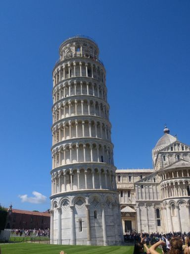 The Leaning Tower of Pisa under a clear blue sky with tourists in the foreground, capturing the iconic architectural marvel in Italy.