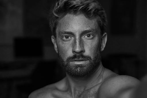 A grayscale portrait of an athletic man with freckles and a beard