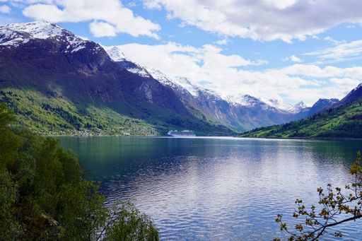 Scenic view of a Norwegian fjord with snow-capped mountains and clear blue sky, reflecting in calm waters.