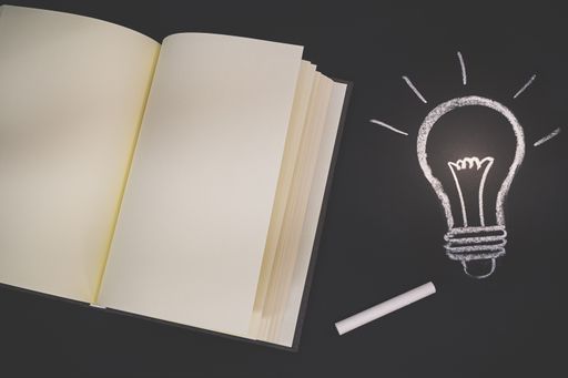 An open book with blank pages and a light bulb drawn by a chalk