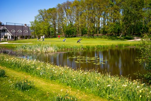 A beautiful view of people playing golf near a water pond at a resort in Lisse on a sunny day