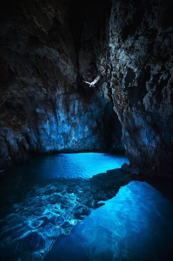 A vertical shot of a person jumping into clear blue water in a cave