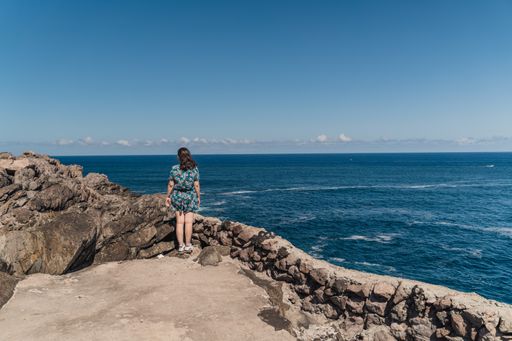 A Caucasian female standing on the edge of a rocky monument looking at the sea in Terceira Island, Azores