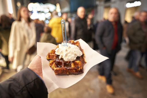 A closeup shot of a person holding a delicious waffle with vanilla ice cream while walking in the street