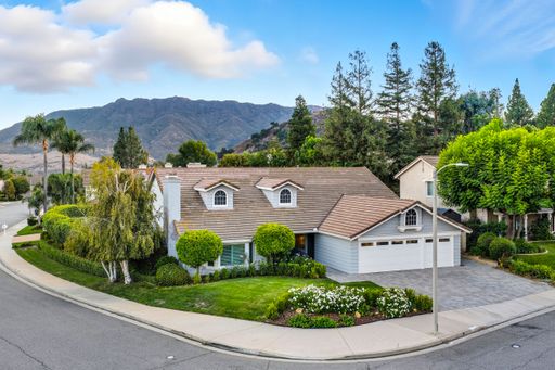 A suburban house with a well-maintained garden and mountain view in the background under a clear blue sky.