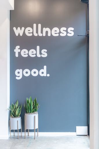 A vertical shot of white text written on the gray wall ’wellness feels good’ under the lights