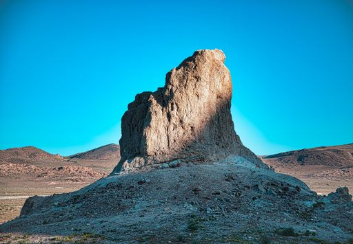A lone pinnacle at sunrise with half of the sun shinning on it against a blue sky.