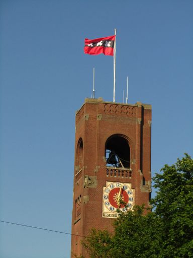 Brick clock tower with the official flag of the Dutch capital city, Amsterdam, Netherlands. Flag flying high on a windy sunny summer day.