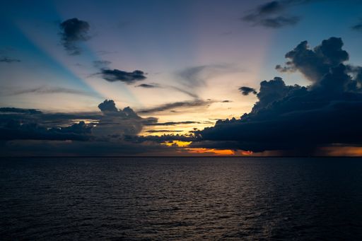 A stunning sunset over a calm ocean with dramatic clouds and vibrant colors in the sky, creating a serene and picturesque scene.