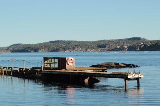 An old pier over the lake water surface with hills in the background against a clear blue sky