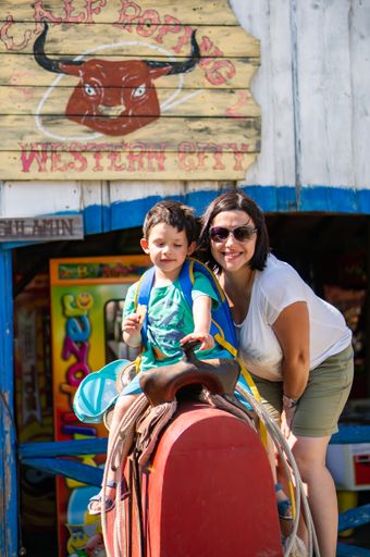 A vertical shot of a woman near a young boy sitting on a horse saddle at the Western City park in Karpacz, Poland