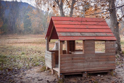A wooden, red-roofed hut with open sides in a forest