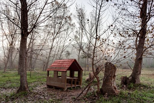 A wooden, red-roofed hut with open sides in a forest