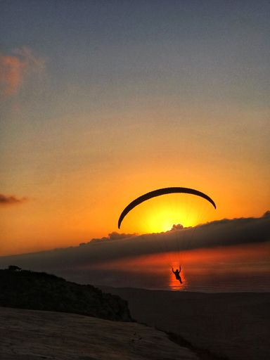 A mesmerizing shot of paragliding in the sky over the lake during sunset