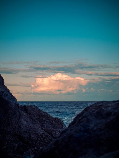 A vertical shot of scenic clouds over the sea behind the rocks