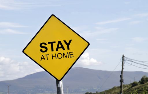 A yellow road sign with the words "Stay at Home" written on it
