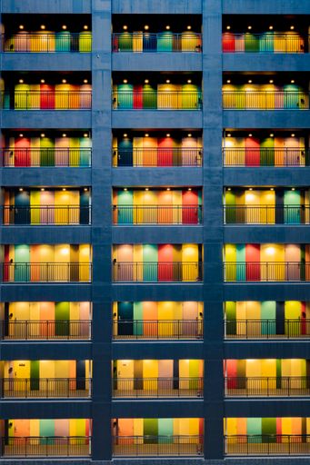 A vertical shot of a building facade with patterned colorful doors and balconies